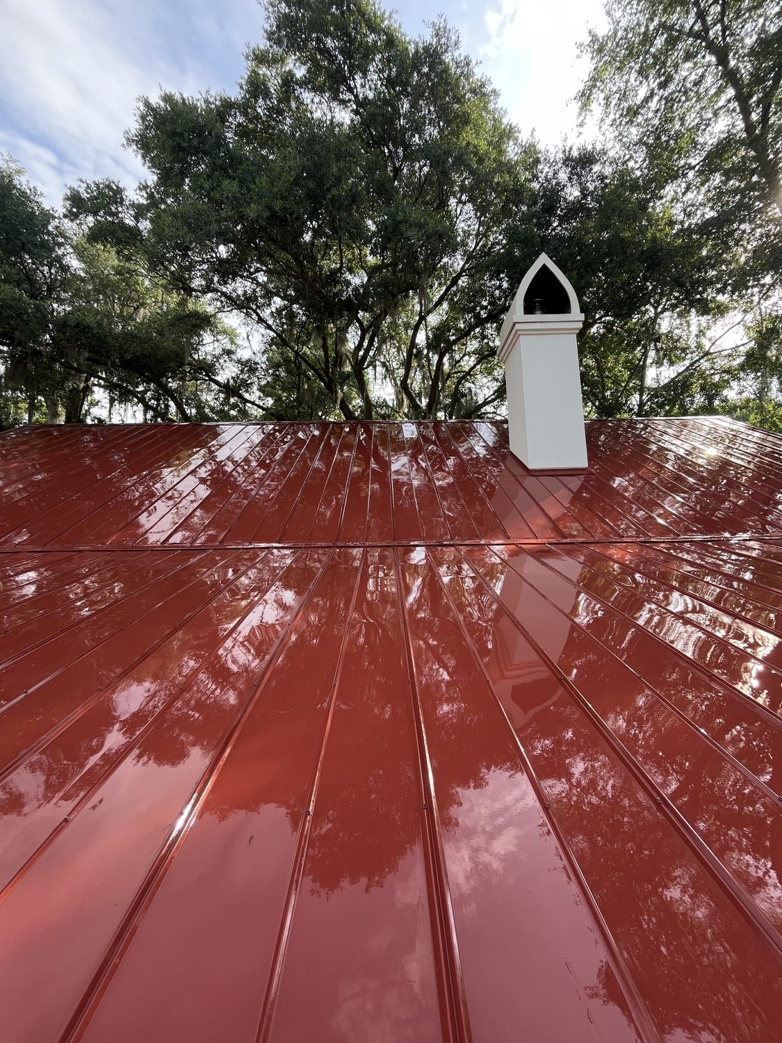 Deep red metal roof restored to a mirror gloss, reflecting the live oaks above
